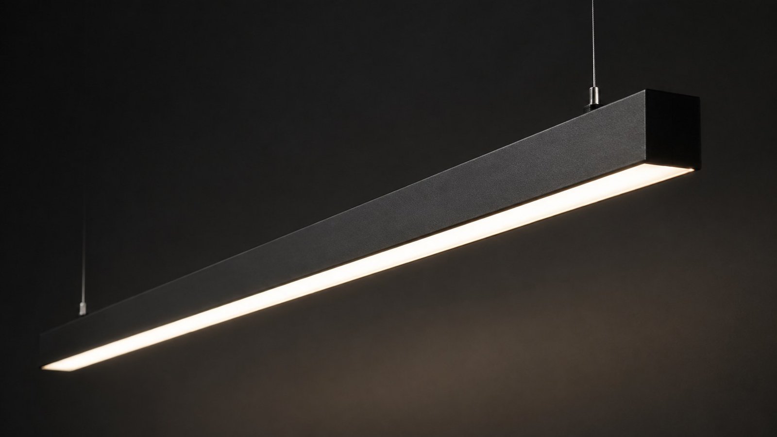 Black suspended linear luminaire with a continuous luminous underside on a dark background